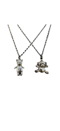 two silver teddy bear necklaces on a black background