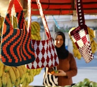 a woman with a crocheted bag in front of a fruit stand